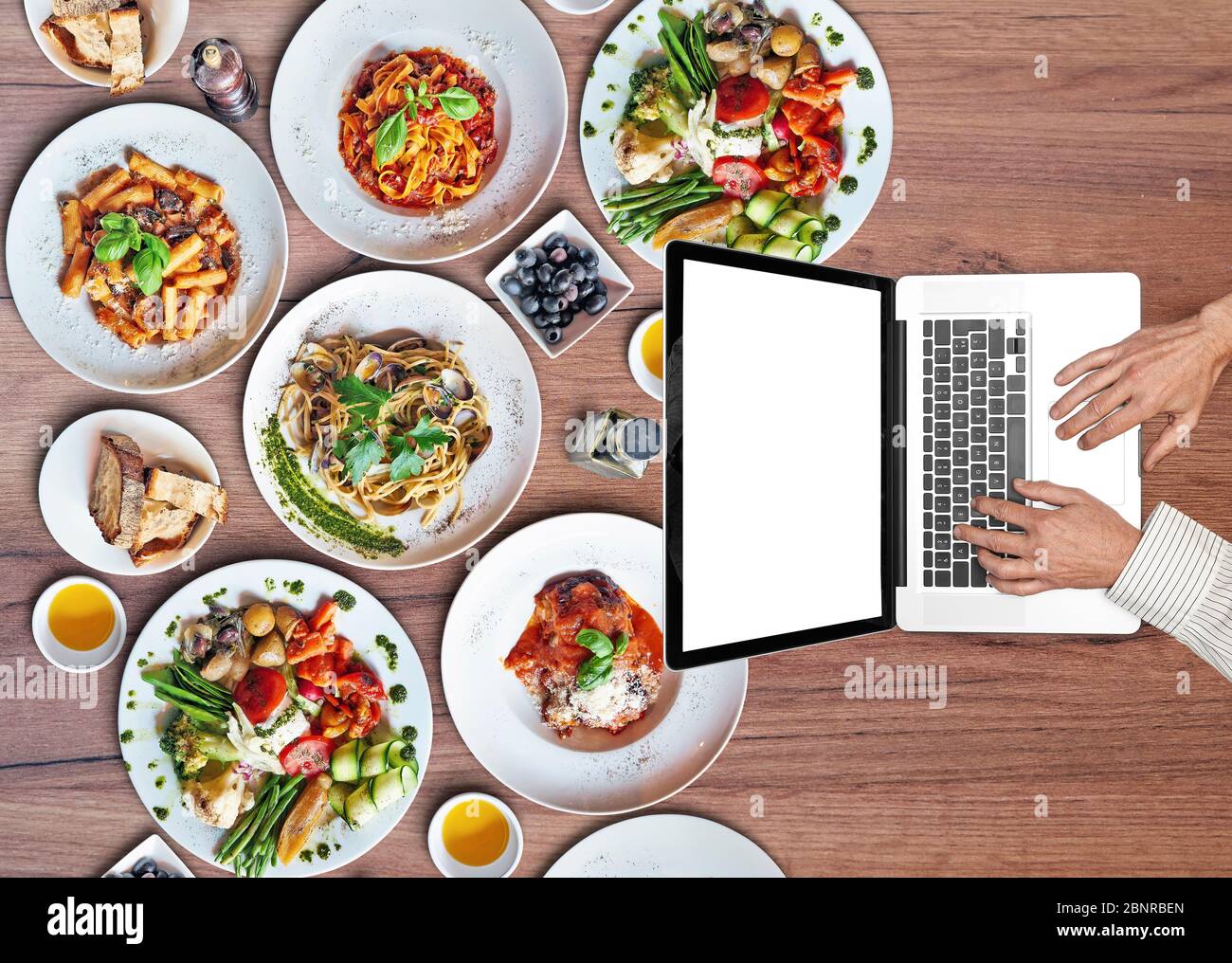 Geschäftsmann arbeitet auf seinem Laptop auf Holztisch mit Tellern von köstlichen italienischen Speisen. Draufsicht Stockfoto