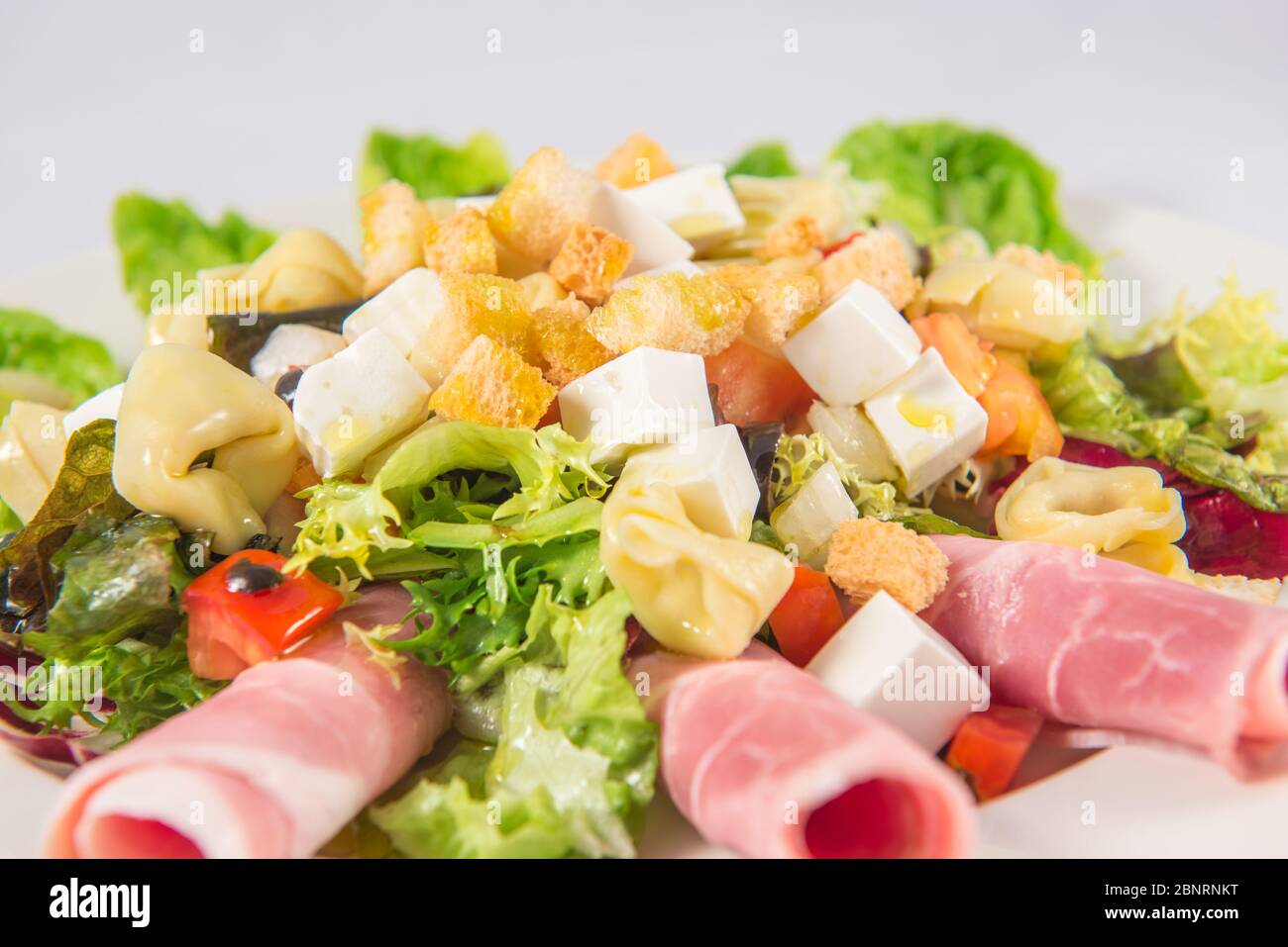 Salat mit Salat, Paprika, Tortellini, frischem Käse, Tomaten, Endive, Schinken und Croutons Stockfoto