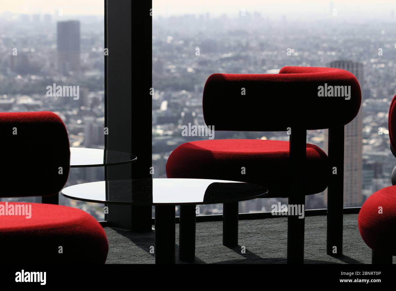 Moderner Cafétisch, der vom Fenster der Lounge eines Wolkenkratzers mit Blick auf die Stadt aufgereiht ist Stockfoto