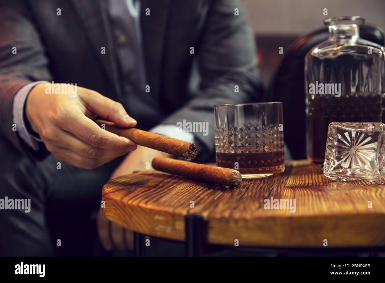 Gentleman nimmt eine Zigarre von einem Holztisch mit Karaffe aus Whisky und Glas Stockfoto