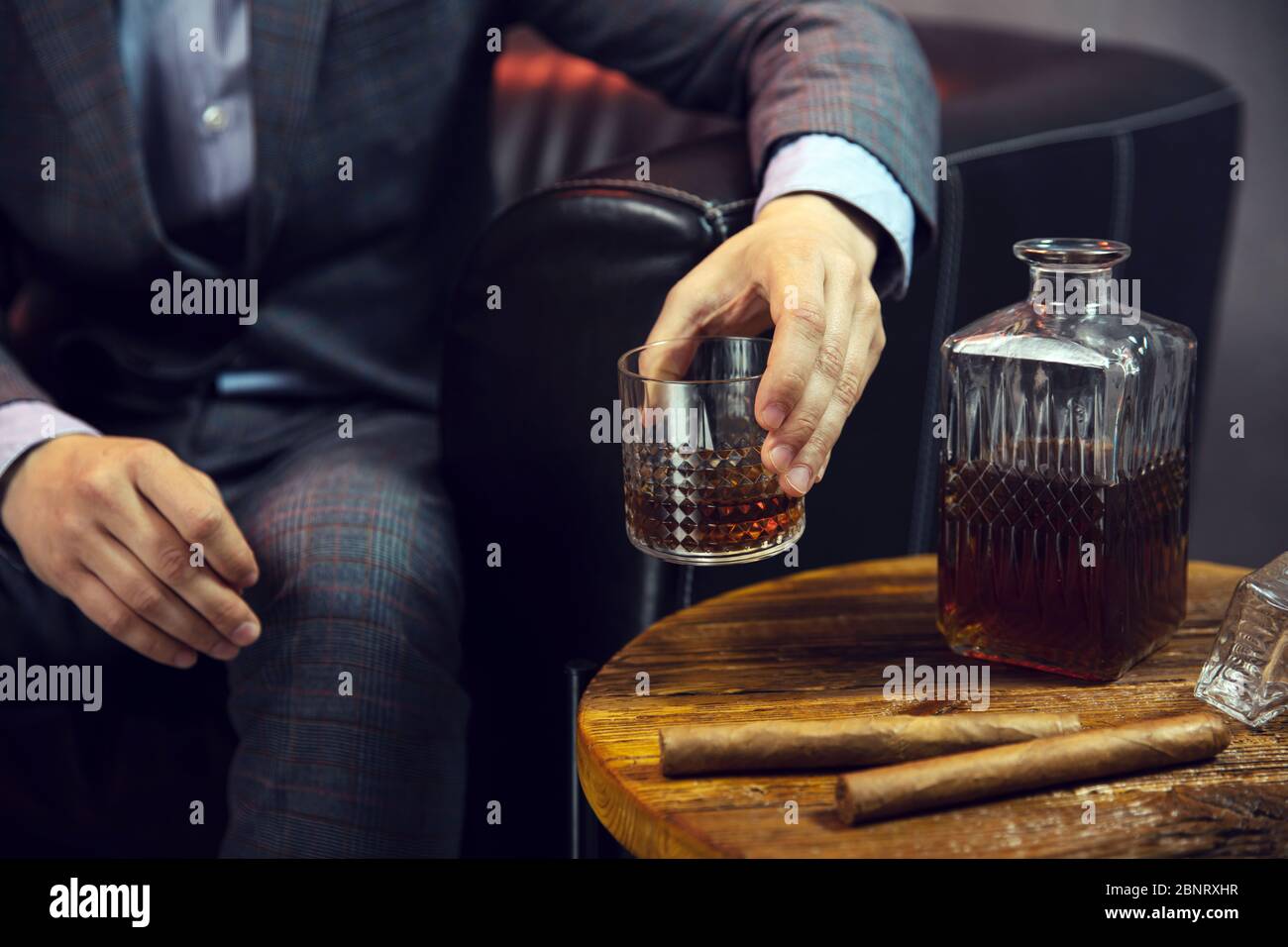Gentleman nimmt ein Glas Whisky und einen Holztisch mit Karaffe Whisky und Zigarren Stockfoto