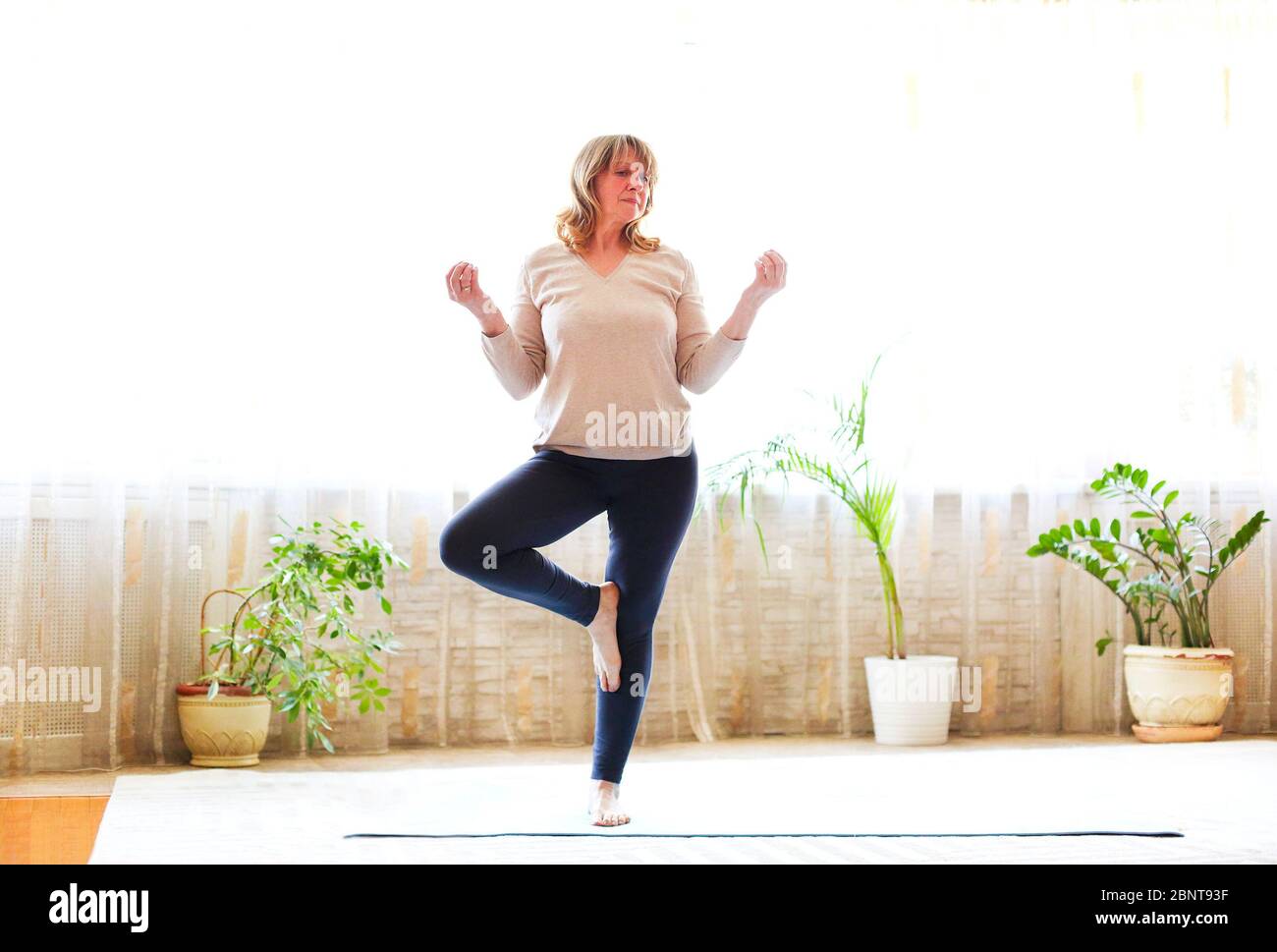 Ganzkörper Erwachsene Frau in Freizeitkleidung Arme heben und Stretching Körper während Yoga auf dem Boden zu Hause Stockfoto