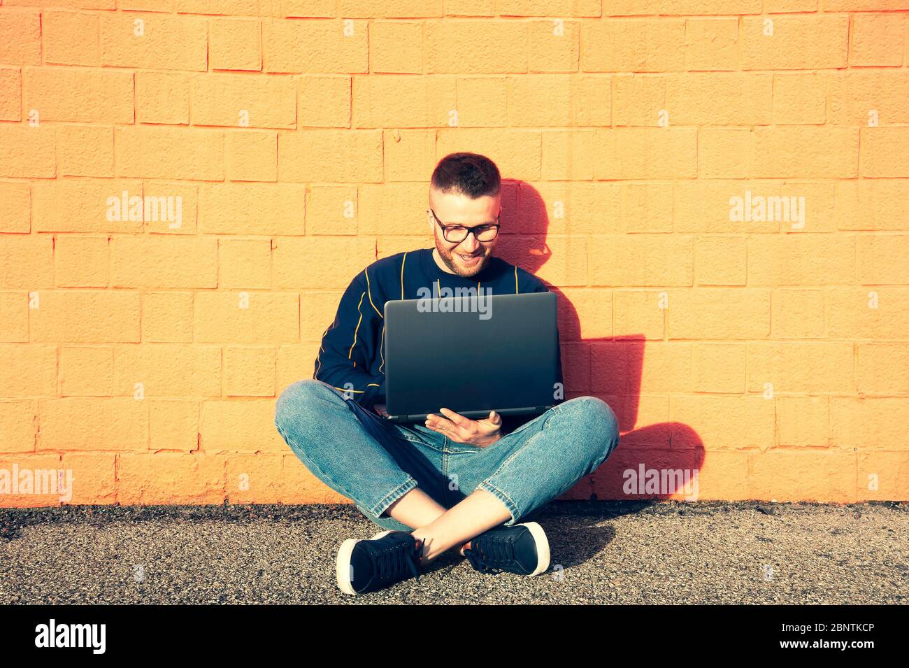 Junge kaukasischen Mann in Freizeitkleidung sitzen mit gekreuzten Beinen auf dem Boden und arbeiten auf Laptop - Freiberufler arbeiten außerhalb Schreiben auf Laptop-Computer, Smart Stockfoto