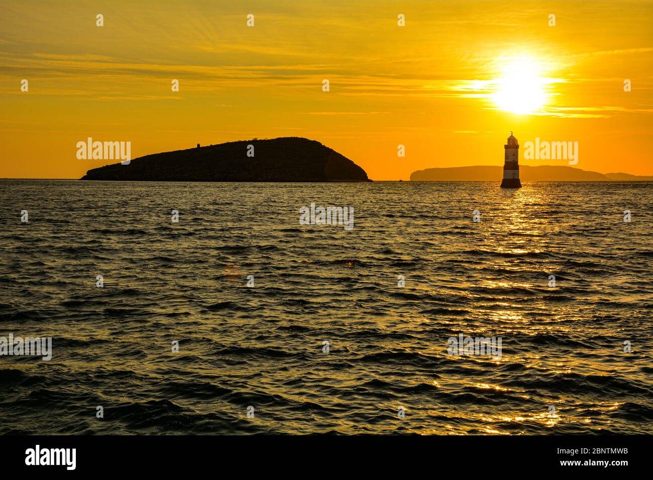Sonnenaufgang über Puffin Island und dem Leuchtturm Trwyn Du in Penmon auf Anglesey in Nordwales Stockfoto