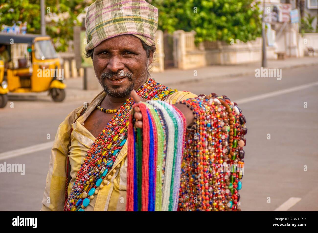 Pondicherry, Indien - 8. Dezember 2013. Ein indischer Straßenhändler, der in der informellen Wirtschaft des Landes arbeitet und versucht, farbenfrohe Perlenhalsketten zu verkaufen. Stockfoto