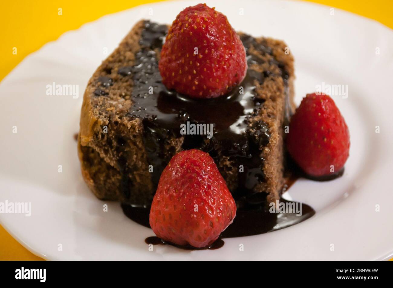 Zwei Schokoladenkuchen mit mehreren Erdbeeren oben in schwarzer Platte auf gelbem Tischhintergrund Stockfoto