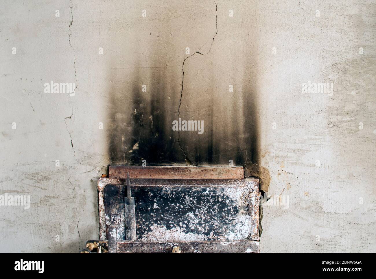 Das Foto zeigt eine graue Lehmwand mit einem Riss und Rauchspuren über der Ofentür, Gefahr, Vernachlässigung Stockfoto