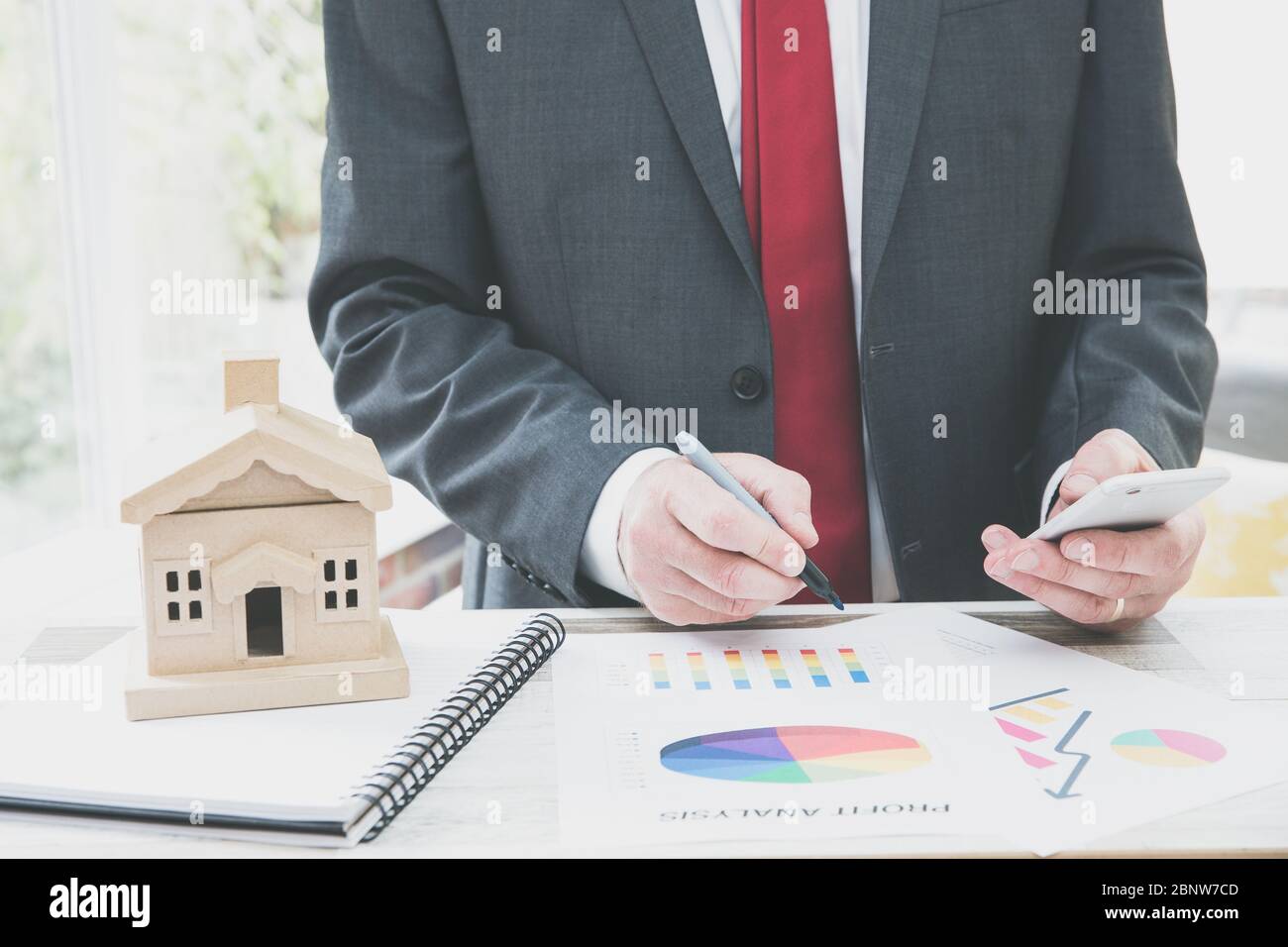 Ein Immobilienentwickler oder Immobilienmakler, der an seinem Schreibtisch arbeitet und den aktuellen Immobilienmarkt mit Diagrammen und Grafiken berechnet oder analysiert. Stockfoto