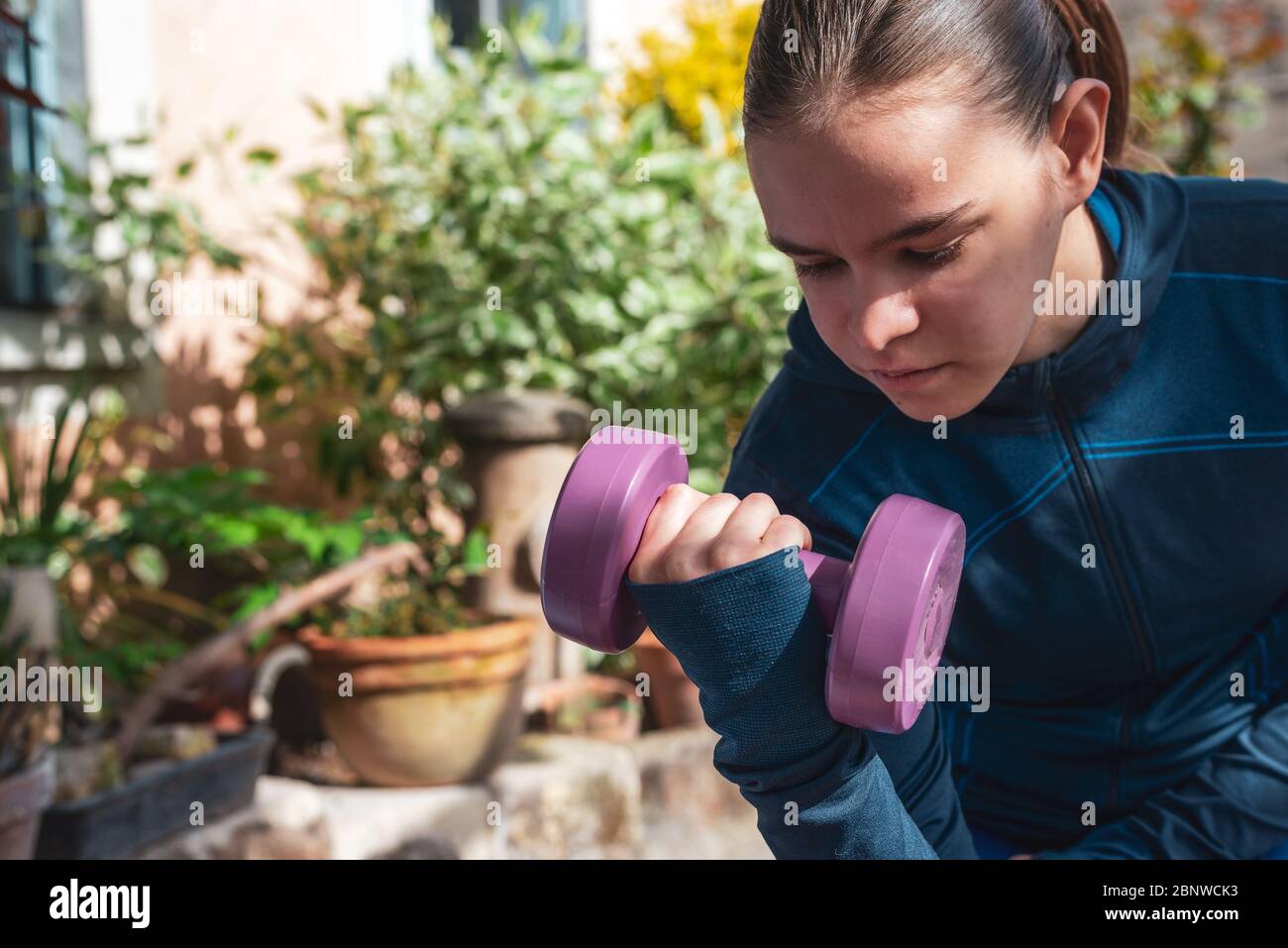 Attraktive junge Frau Athlet Arbeit im Garten mit Gewichten in Sportkleidung gekleidet...Vergangenheit Zeit hile beschränkt. Stockfoto