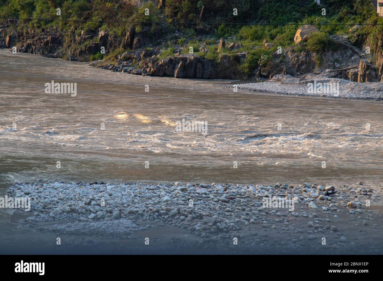 Landschaft des Flusses Alaknanda und seine Stein- und Kornküste, die während der goldenen Stunden des Sonnenuntergangs glänzen, verschwommener Blick durch die Landschaft, 5K Stockfoto