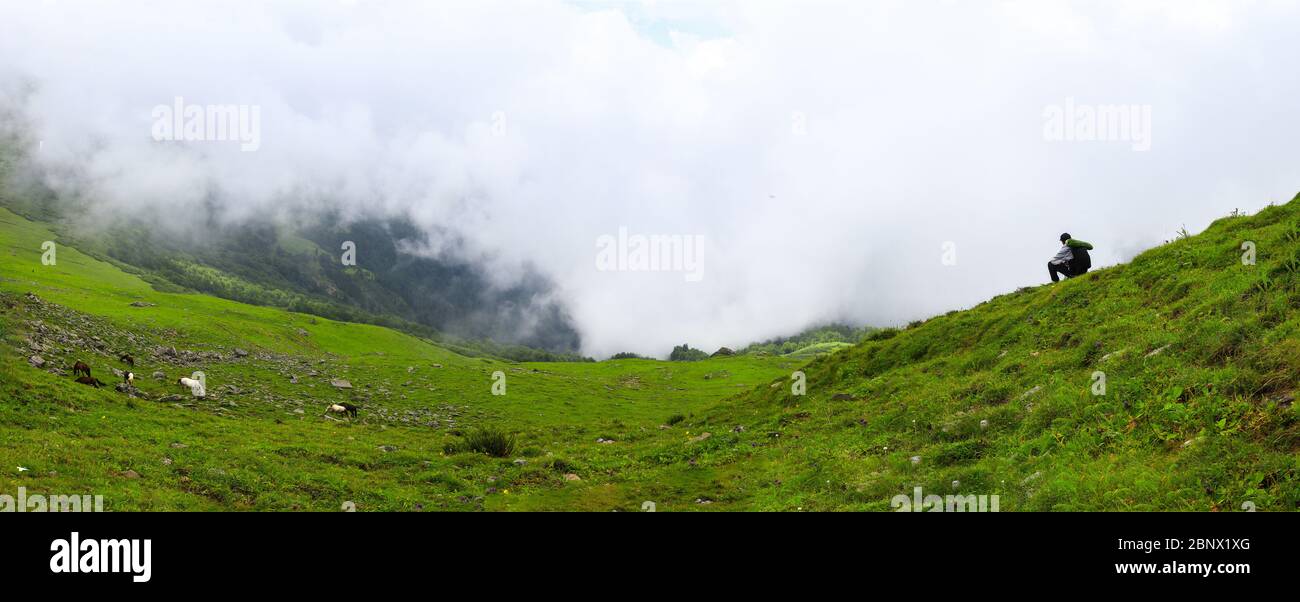 Schöne 8K Ultra HD Panorama, SITZT EINE Person auf den riesigen grünen Wiesen von Chanderkhani, wo Wolken schweben und Pferde grasen bergab, was die Stockfoto