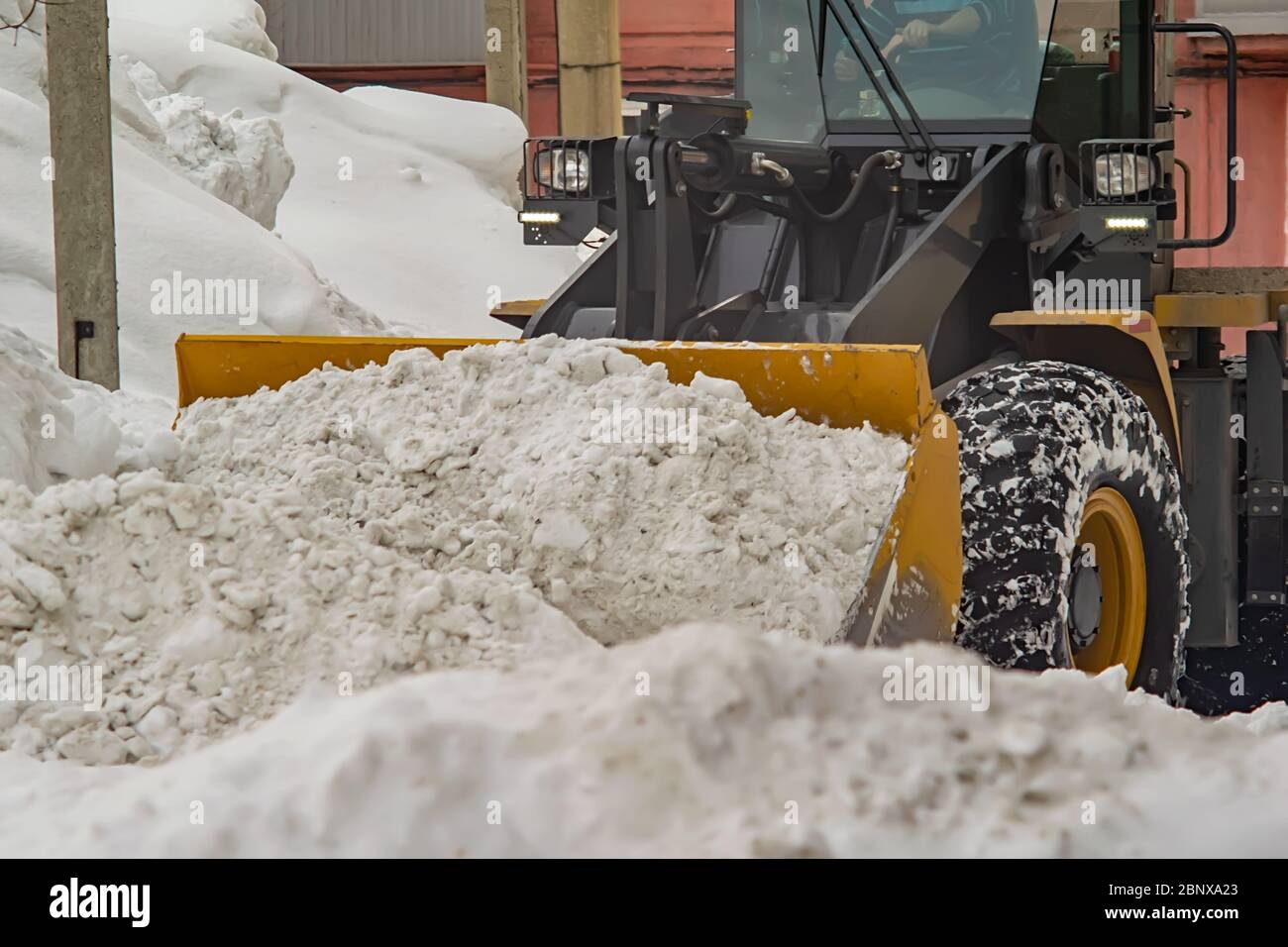 Traktor, Grader entfernt einen Haufen Schnee im Hof eines Wohngebäudes Stockfoto
