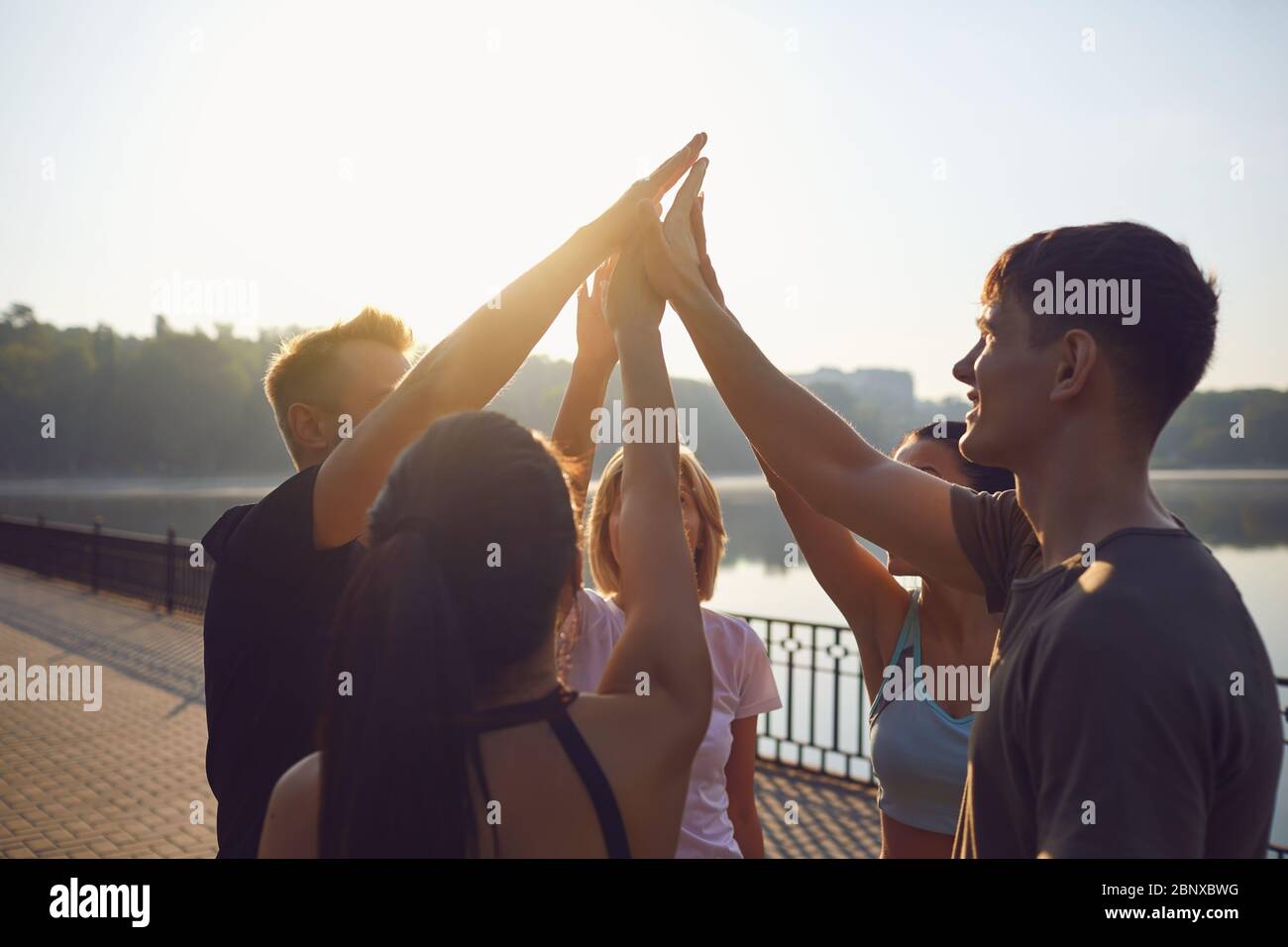 Eine Gruppe junger Menschen in Sportbekleidung legte sich die Hände zusammen, während sie morgens im Morgengrauen in einem Park standen. Ein Team von Sportlern trainiert zusammen. Stockfoto
