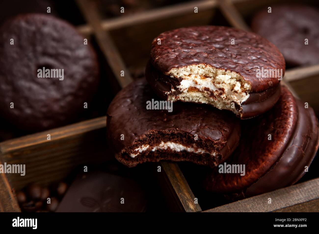 Ein paar süße Choco Pie Desserts auf einem hölzernen Hintergrund unter verstreuten Kaffeebohnen.Schokolade und klassisches Dessert Choco Pie Stockfoto