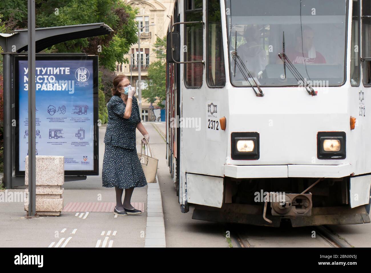 Belgrad, Serbien - 12. Mai 2020: Eine ältere Frau, die eine Gesichtsmaske und Handschuhe trägt, kommt in den öffentlichen Nahverkehr Stockfoto