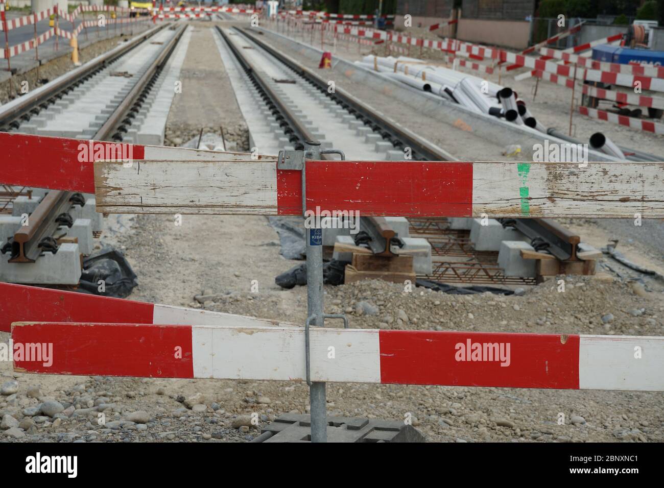 Bau einer Straßenbahn, Einbettung von Metallschienen in einen Betonsockel mit einer Barrieresteele im Vordergrund aus Sicherheitsgründen. Stockfoto