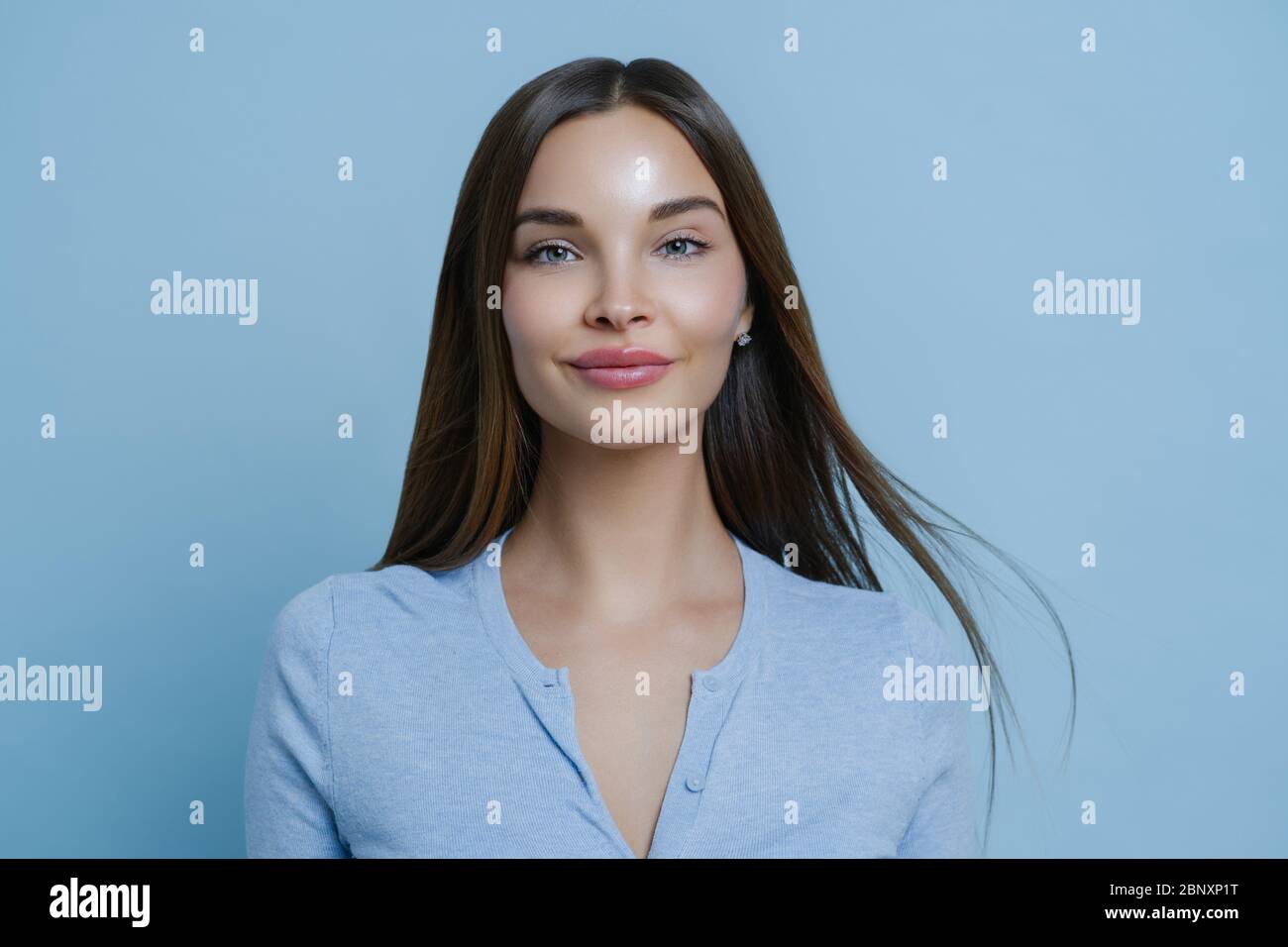 Indoor-Porträt von hübschen Frau fühlt sich glücklich und unbeschwert während des Tages frei, hat lange glatte Haare, trägt blauen Pullover, genießt positive Konversation, Stan Stockfoto