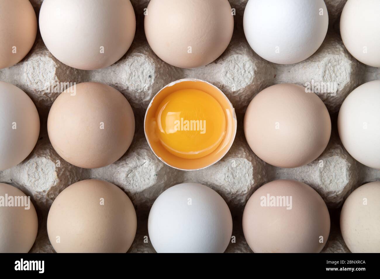 Hühnereier in Bio-Verpackung Nahaufnahme. Ei halb gebrochen unter anderen Eiern. Food-Fotografie Stockfoto