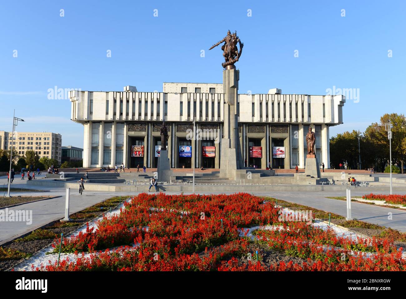 Kirgisische Nationalphilharmonie in Bischkek, Kirgisistan, benannt zu Ehren von Toktogul Satylganov und in der Sowjetzeit im brutalistischen Stil erbaut. Rote Blumen Stockfoto