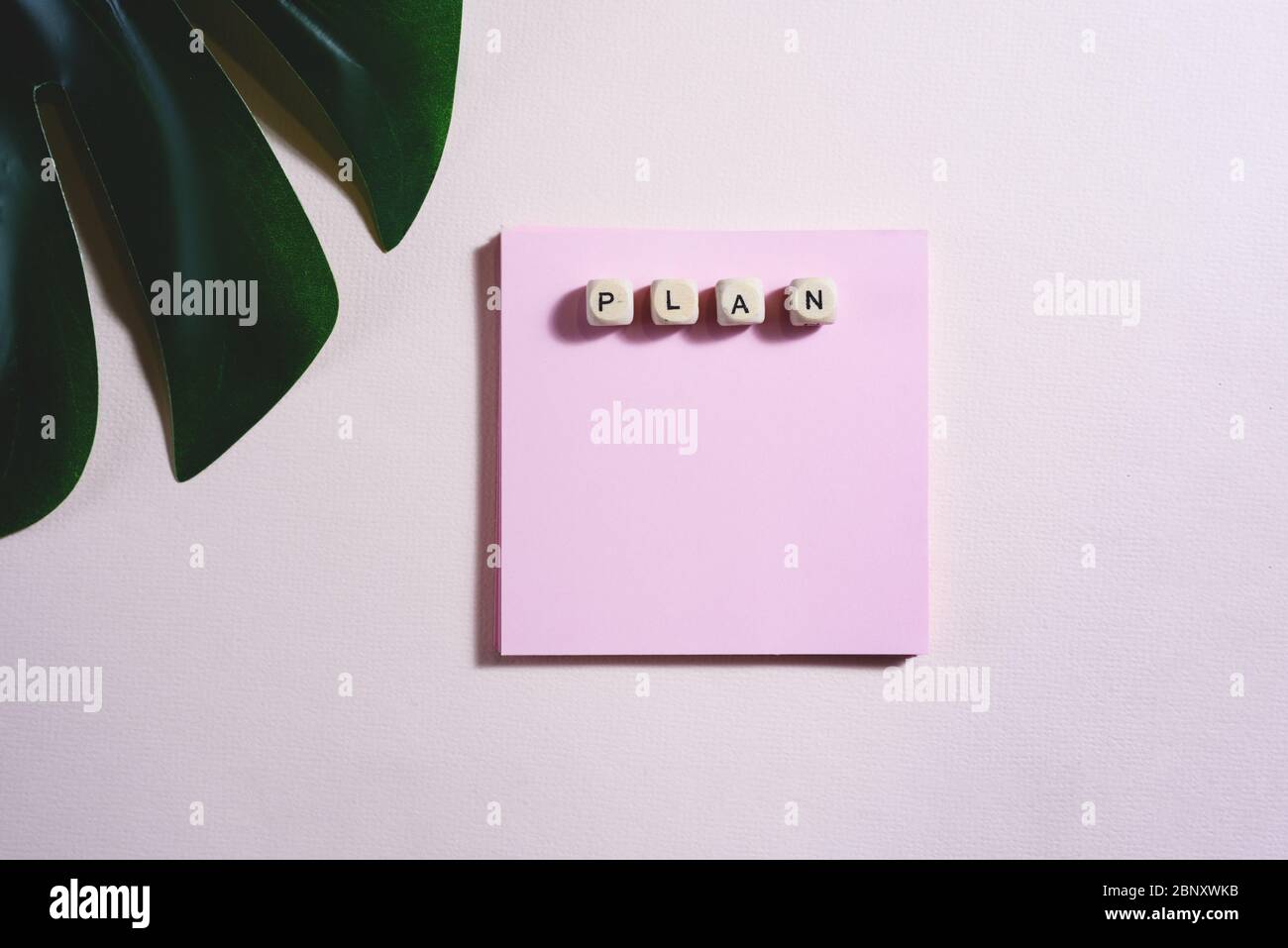 Flaches Lay von leeren leeren und hölzernen Ziegelsteinen mit Schild Plan darauf und teilweise ein Blatt Monstera auf dem rosa Hintergrund. Stockfoto