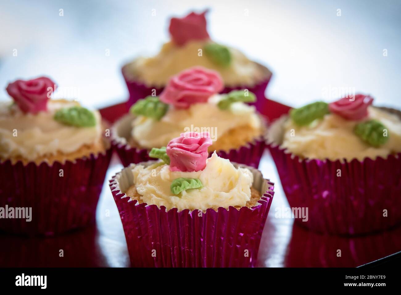 Cupcakes in Folienhaltern mit Buttereisung und liebhabenden Rosen und Blättern Stockfoto