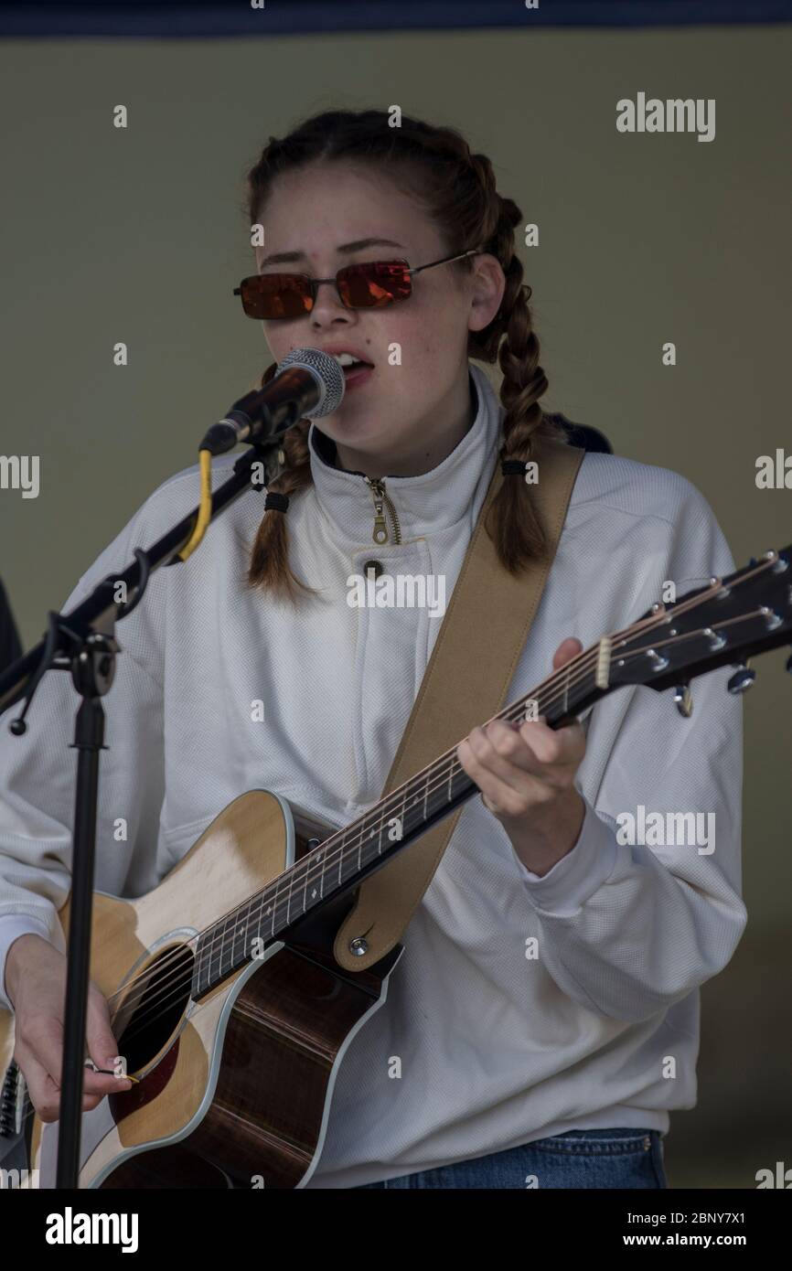 Teenager-Mädchen, mit cooler Sonnenbrille und Zöpfen, die Gitarre spielen und in der Band singen, bei einem Konzert im Outdoor Stockfoto