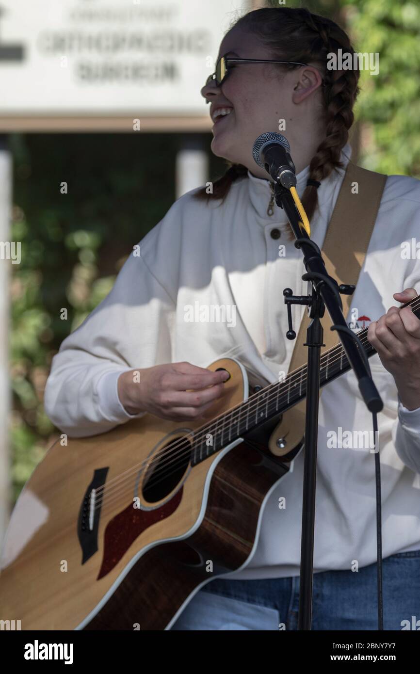 Teenager-Mädchen, mit cooler Sonnenbrille und Zöpfen, die Gitarre spielen und in der Band singen, bei einem Konzert im Outdoor Stockfoto