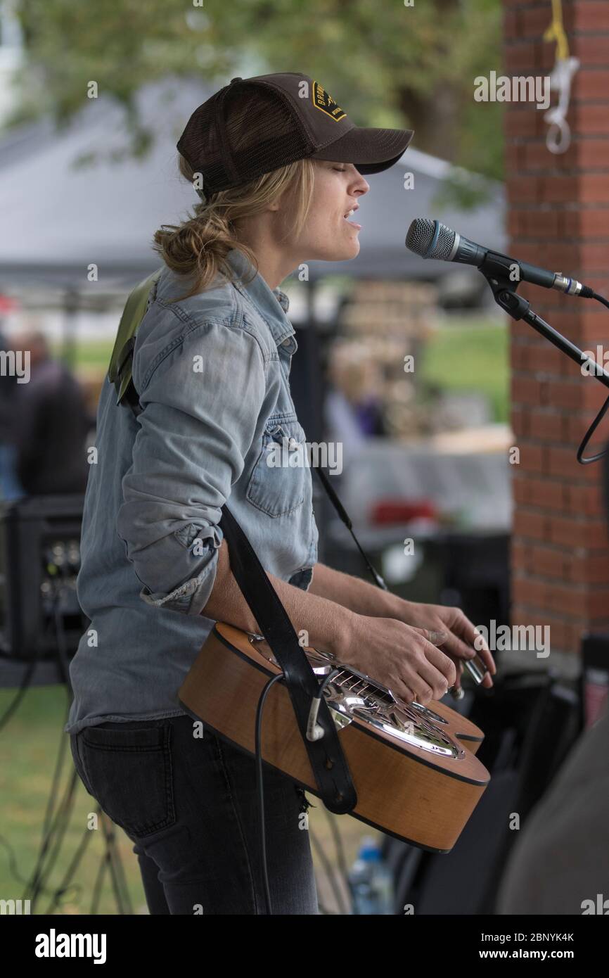 Hübsche, blonde Frau, die Lap-Akustikgitarre spielt und bei einem Konzert im Freien singt. Tragen einer Kugelmütze Stockfoto