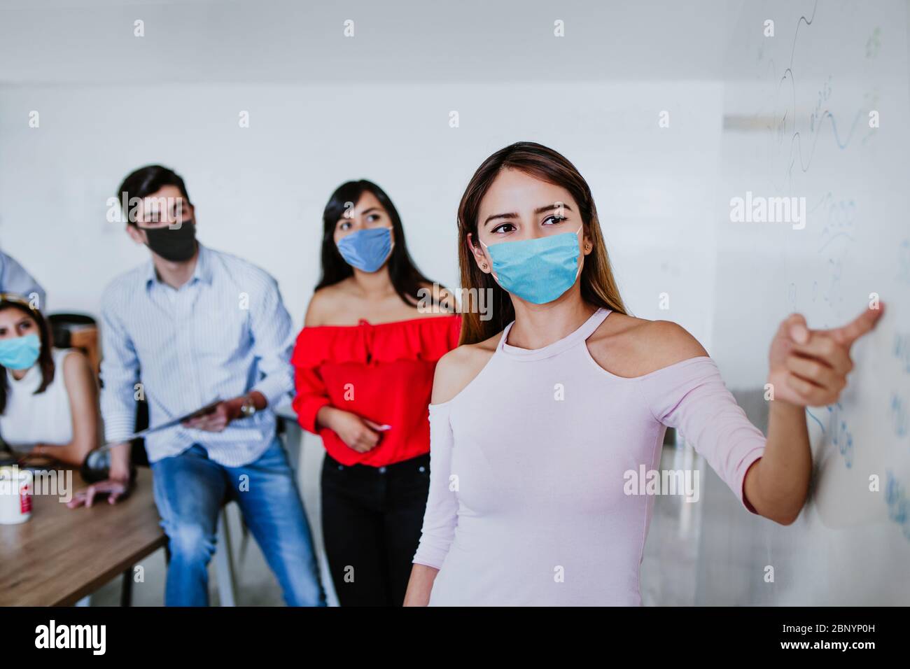 Lateinische Frau, die im Business Office oder Coworking arbeitet, während sie medizinische Gesichtsmaske trägt, um in neuen normalen Situationen soziale Distanz zu bewahren und zu preve Stockfoto