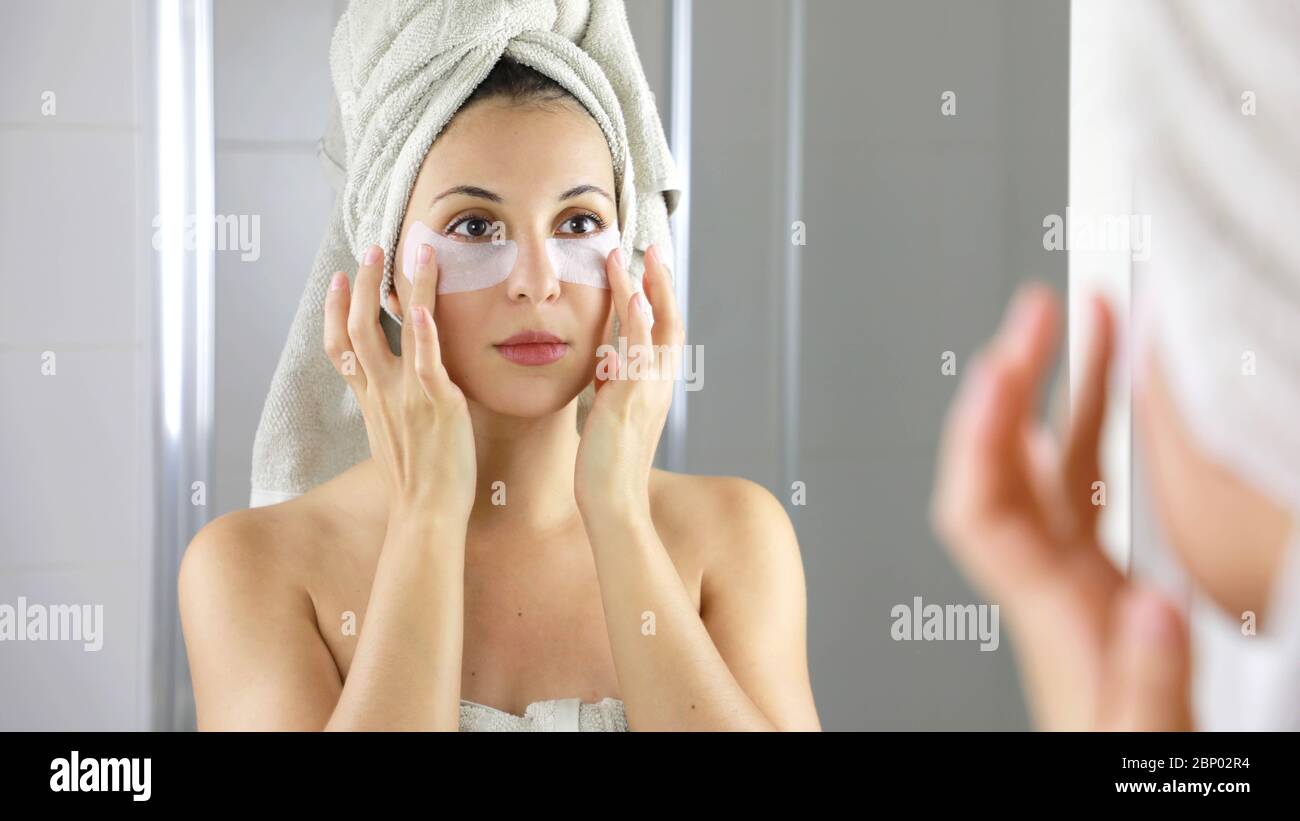 Beauty Frau Anwendung Anti-Müdigkeit unter den Augen Maske suchen sich in den Spiegel im Badezimmer. Hautpflege Mädchen berühren Flecken von Stoff Maske unter den Augen Stockfoto