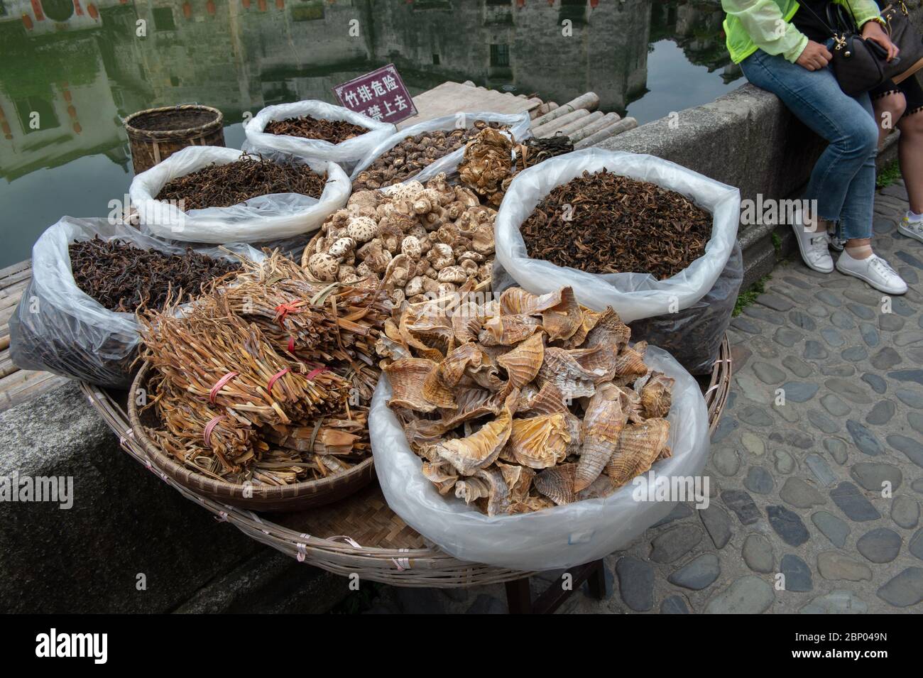 Straßenhändler verkaufen Pilze und Bündel von Bambussprossen an der Seite einer Kopfsteinpflasterstraße im Dorf Hongcun, China. Stockfoto