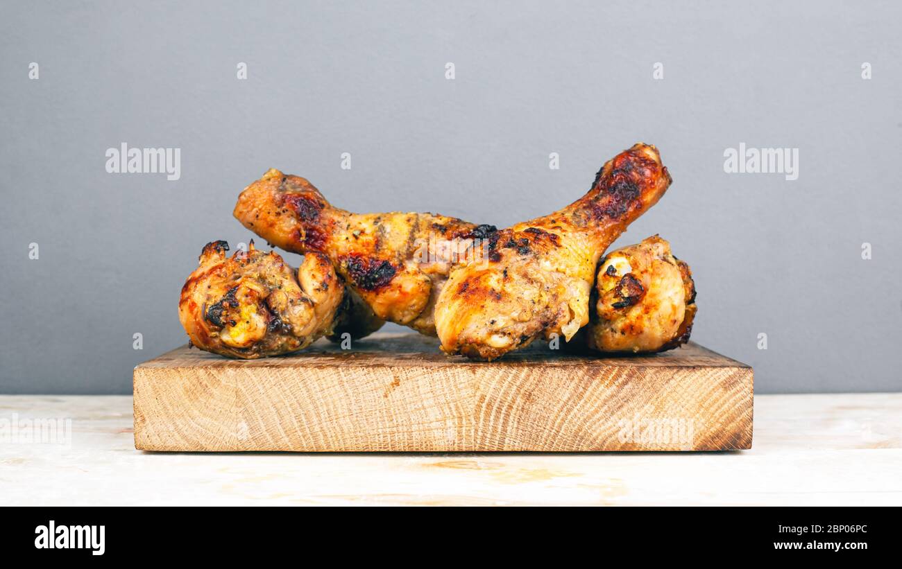 Gegrillte Hähnchenbeine auf einem Holzteller auf grauem Hintergrund. Saftiges knuspriges Hähnchen, herzhaftes Mittagessen im Freien zubereitet, B-B-Q. Stockfoto