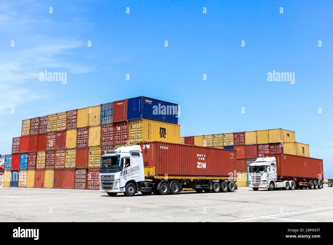 LKW beladen mit einem Zim Shipping Container mit Stapeln verschiedener Container Marken im Hintergrund. Stockfoto
