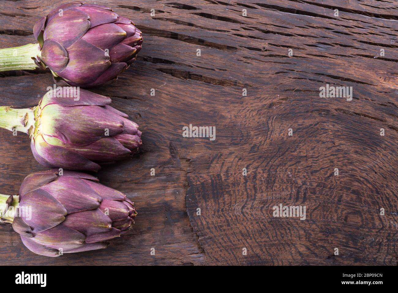 Grüne und violette Artischocke blühen essbare Knospen auf Holzhintergrund. Stockfoto