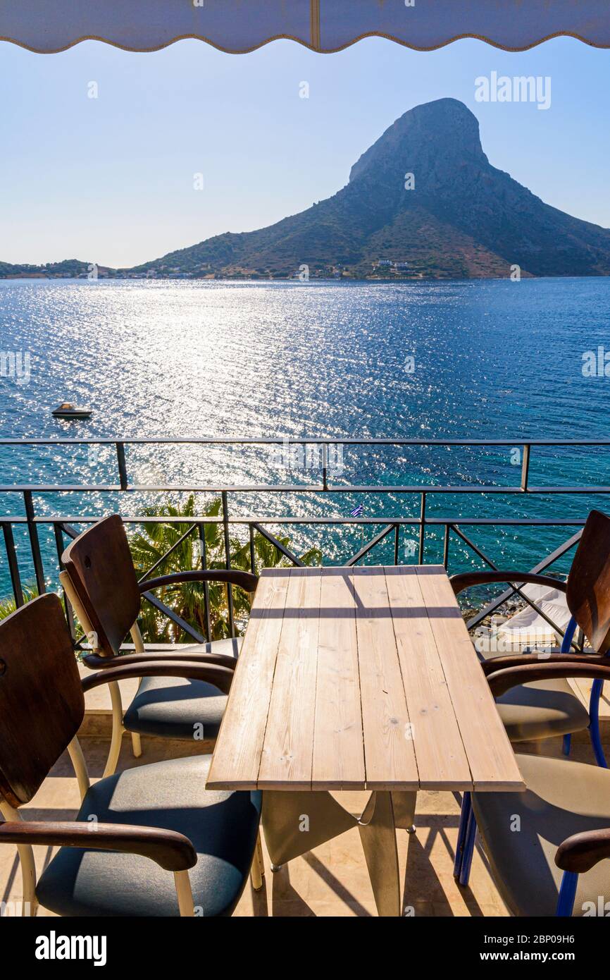 Meerblick auf die Insel Telendos über einen Tisch und Stühle auf einem Balkon im Ferienort Masouri, Kalymnos, Dodekanes, Griechenland Stockfoto