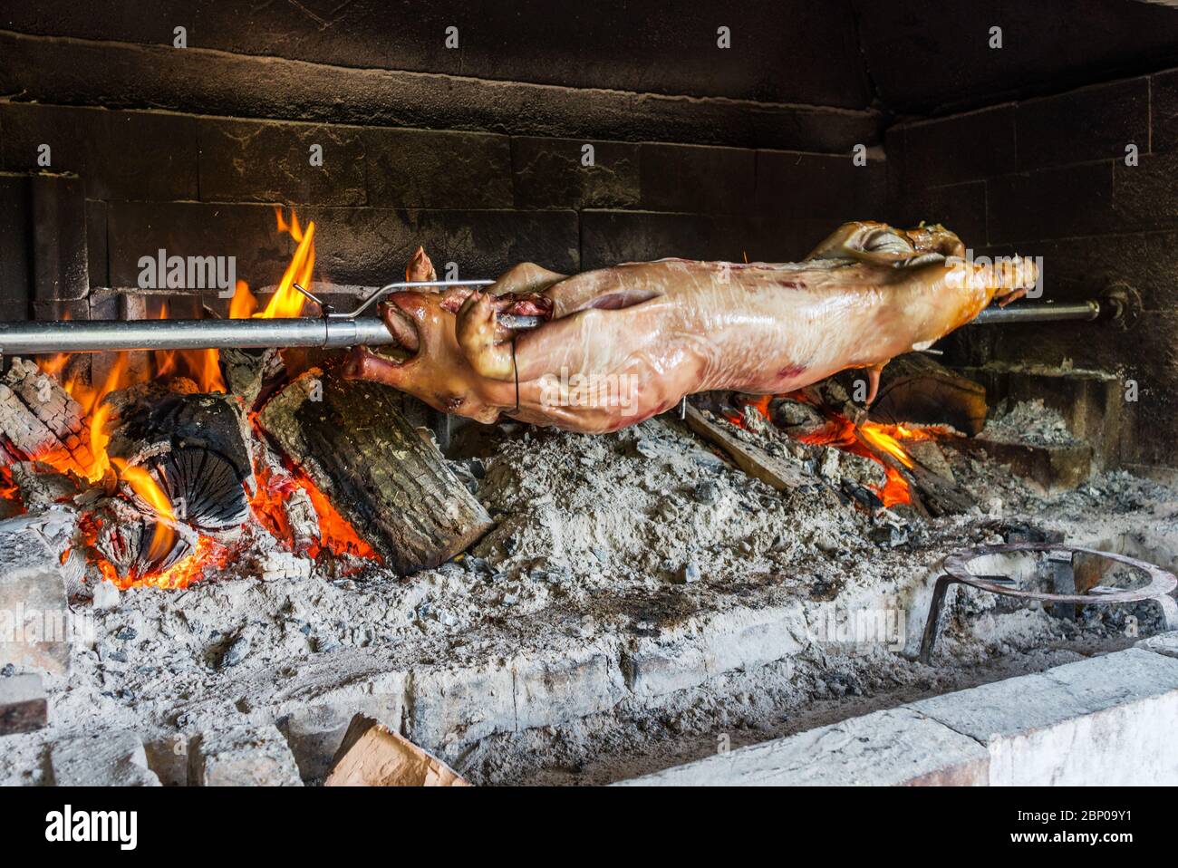 Das saugende Schwein wird auf einem Spieß über offenem Feuer auf den Holzofen geröstet. Stockfoto