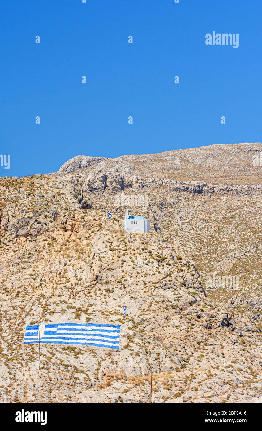 Weiße griechische Kirche und Flagge Griechenlands auf den trockenen Hügeln der Insel Kalymnos, Dodekanes, Griechenland gemalt Stockfoto