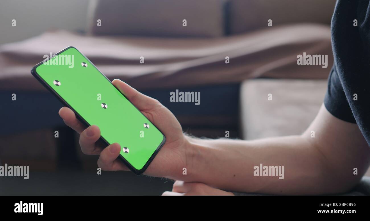 Nahaufnahme junger Mann sitzen auf einer Couch und schauen etwas zu Auf einem Smartphone mit grünem Bildschirm Stockfoto