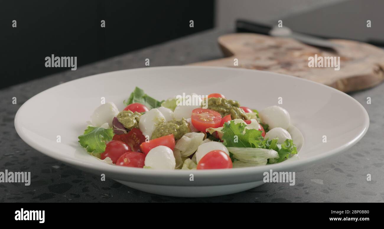 Salat mit gemischtem Gemüse, Tomaten und Mozzarella in einer weißen Schüssel auf einer Betonplatte mit Pesto bestreichen Stockfoto