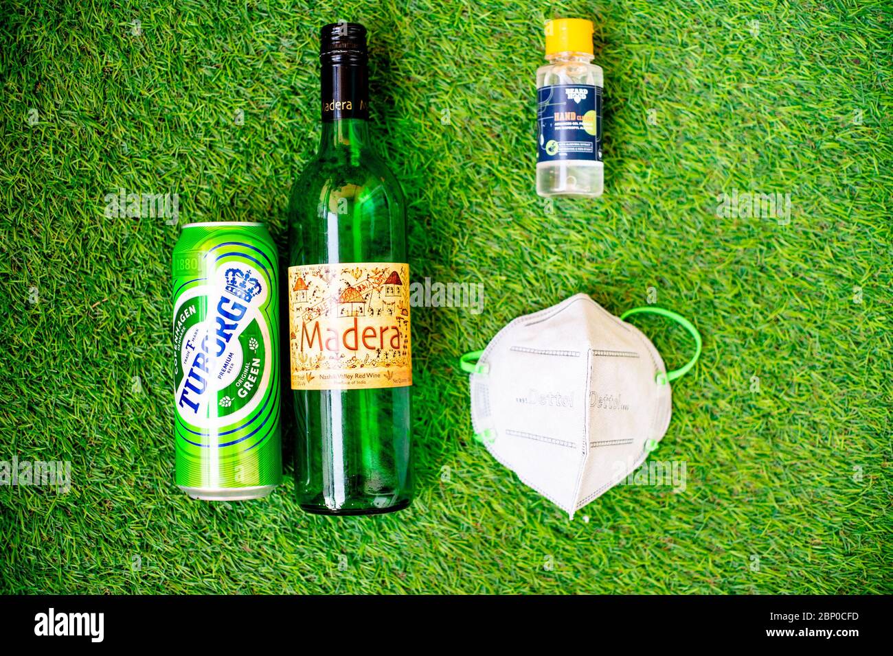Flatlay von Alkohol Liquor Flaschen auf Gras mit einer Maske und Desinfektionsmittel zeigt die Lieferung nach Hause und Kauf von Alkohol und Likör während Coronavius Stockfoto