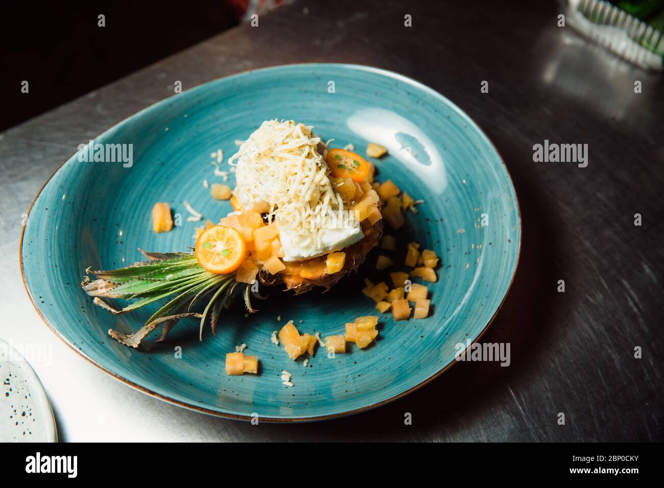 Frisch zubereiteter Salat liegt in der Ananas, die längs geschnitten und mit geriebenem Käse bestreut wird. Alles sieht sehr appetitlich aus. Stockfoto