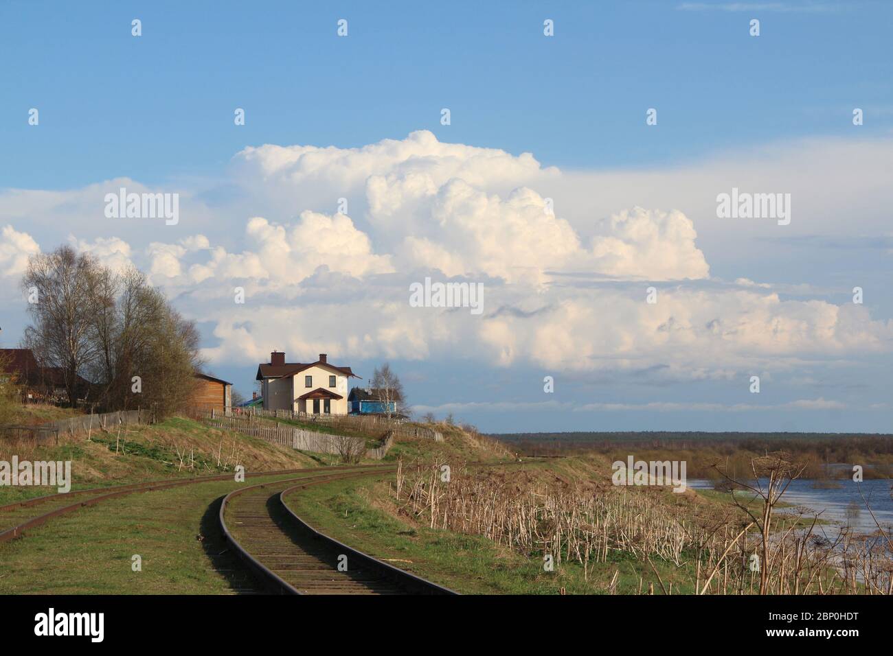 Schöne Landschaft mit dem Horizont und mit einem weißen Haus auf einem Hügel. Landschaft im Frühjahr mit trockenen und jungen grünen Gras. Weiße Cumulus Wolken gegen den blauen Himmel. Ferienhaus am Rande des Dorfes neben der Eisenbahn. Stockfoto