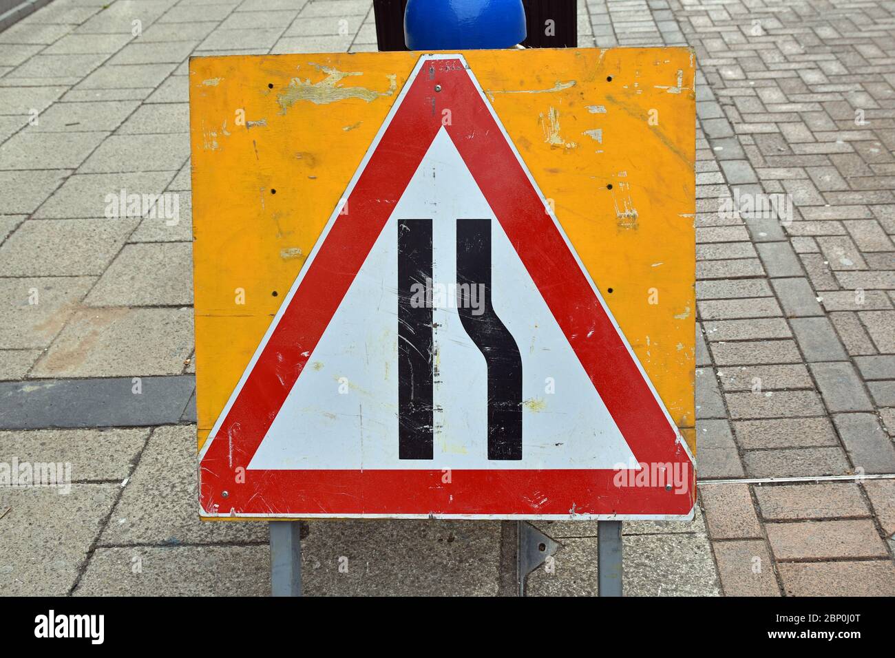 Dreieckige rot-weiße Straßenschild UK Road Engerging auf der rechten Seite, auf gelber Tafel. Ramponiert aussehende Schild auf asphaltierter Straße, städtische Umgebung. Stockfoto