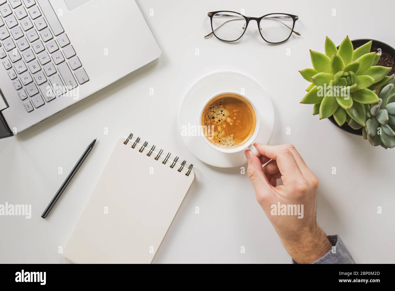 Die Hand des Mannes hält eine Tasse Kaffee an seinem Arbeitsplatz Stockfoto