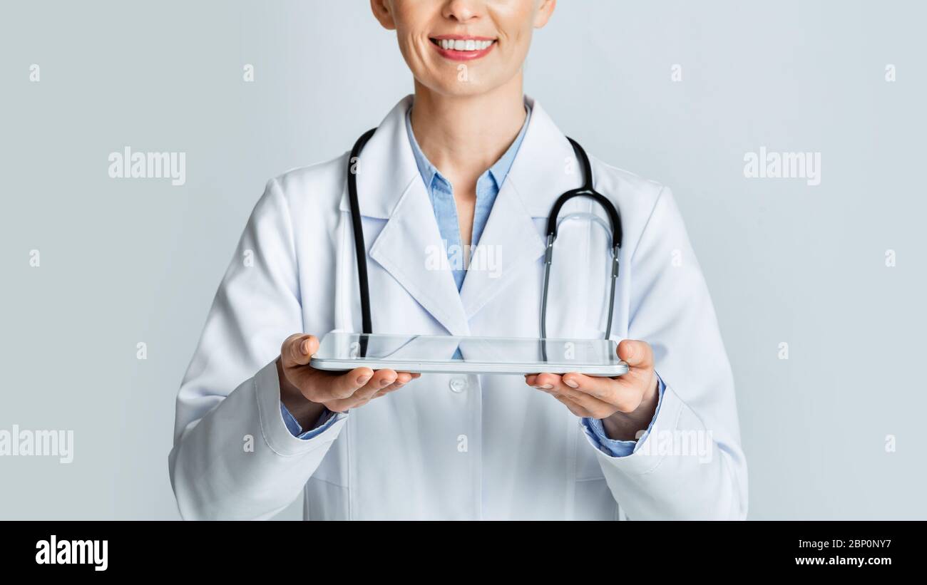 Moderne Medizin Dienstleistungen und Bewertungen. Lächelnde Frau Arzt hält Tablet vorsichtig in den Händen Stockfoto