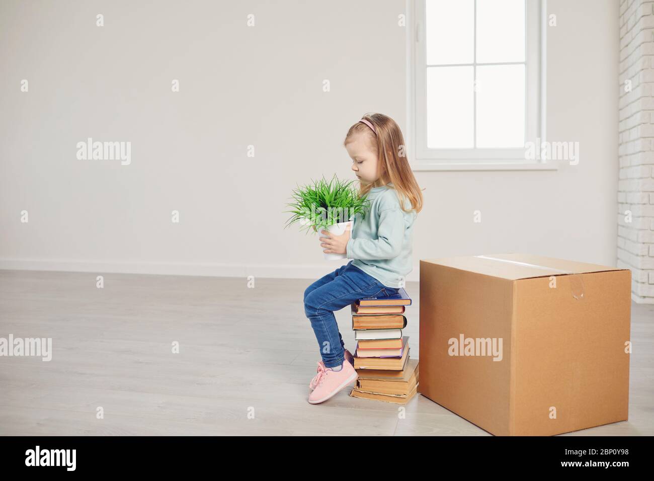 Ein Mädchen mit einer Blume sitzt auf den Kisten für den Umzug in ein neues Haus. Stockfoto