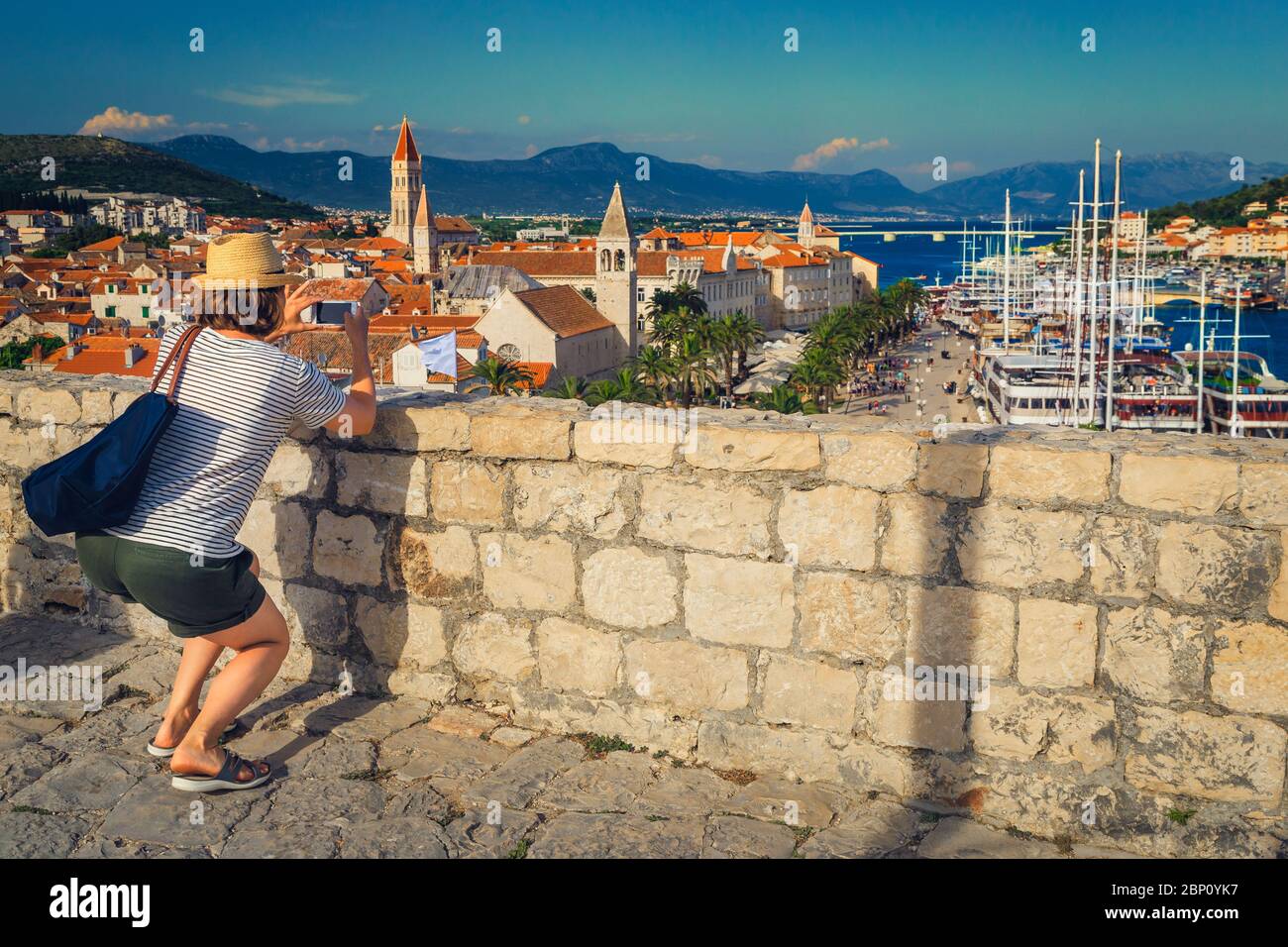 Hübsche Frau, die ein Foto mit dem Telefon aus dem Schloss. Glückliche Reisende Frau mit Smartphone, die Reise Bilder in Trogir Altstadt aus dem Turm Stockfoto