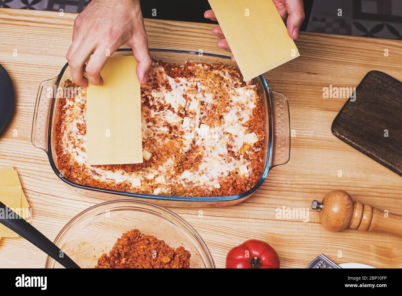 Die Hände des Menschen machen Lasagne Schichten in Glastablett, Stockfoto