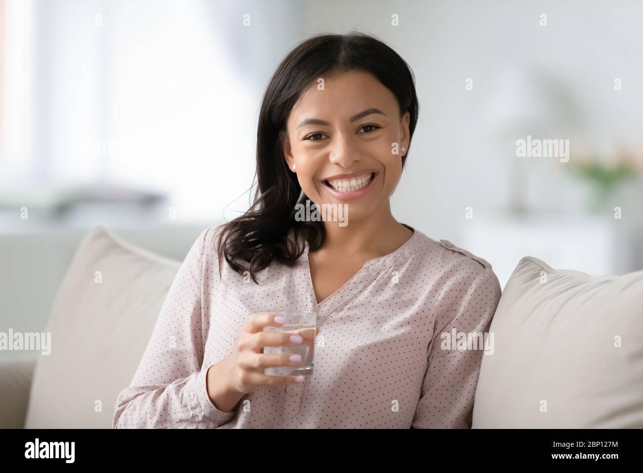 Frau auf dem Sofa sitzend, Glas Wasser haltend fühlt sich gesund an Stockfoto