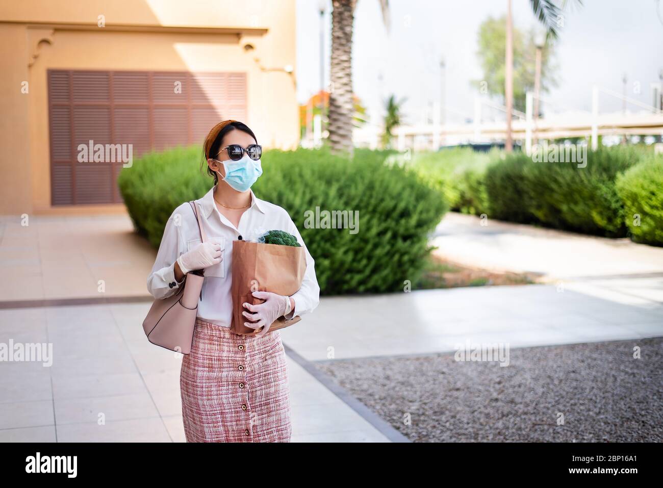 Asiatische Frau, die Einkaufstasche mit Lebensmitteln trägt, während sie Maske und Handschuhe trägt, um die Ausbreitung des Virus während der Coronavirus-Pandemie zu verhindern Stockfoto